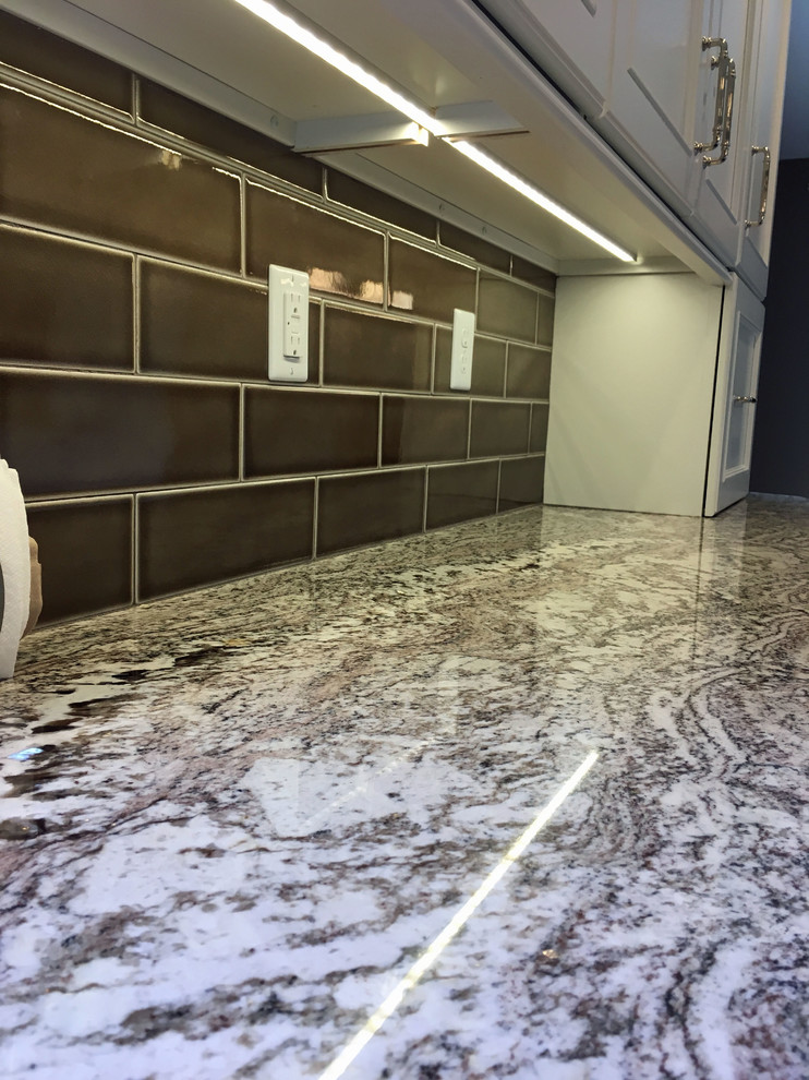 Large transitional l-shaped vinyl floor and beige floor eat-in kitchen photo with a double-bowl sink, recessed-panel cabinets, white cabinets, granite countertops, brown backsplash, ceramic backsplash, stainless steel appliances and an island