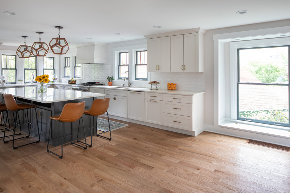 Transitional l-shaped medium tone wood floor and brown floor eat-in kitchen photo with a drop-in sink, shaker cabinets, white cabinets, quartzite countertops, white backsplash, subway tile backsplash, stainless steel appliances, an island and white countertops