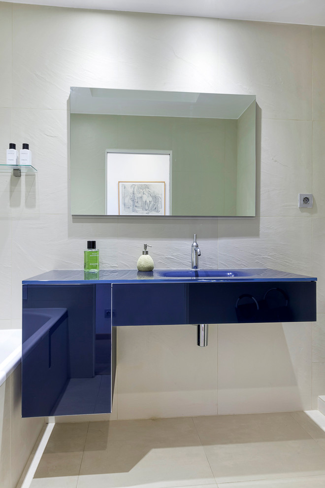 Mid-sized contemporary kids bathroom in Paris with a console sink, glass-front cabinets, blue cabinets, glass benchtops, a freestanding tub, beige tile, ceramic tile, beige walls and ceramic floors.