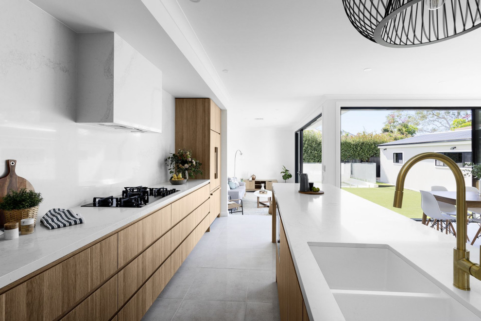Photo of a contemporary galley open plan kitchen in Sydney with a submerged sink, light wood cabinets, white splashback, stone slab splashback, integrated appliances, an island, grey floors and white worktops.