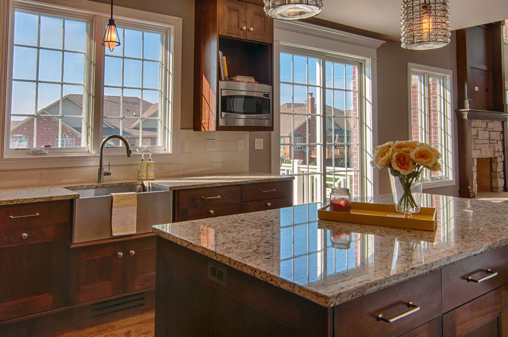 Mid-sized transitional u-shaped dark wood floor eat-in kitchen photo in Chicago with a farmhouse sink, recessed-panel cabinets, medium tone wood cabinets, granite countertops, beige backsplash, ceramic backsplash, stainless steel appliances and an island