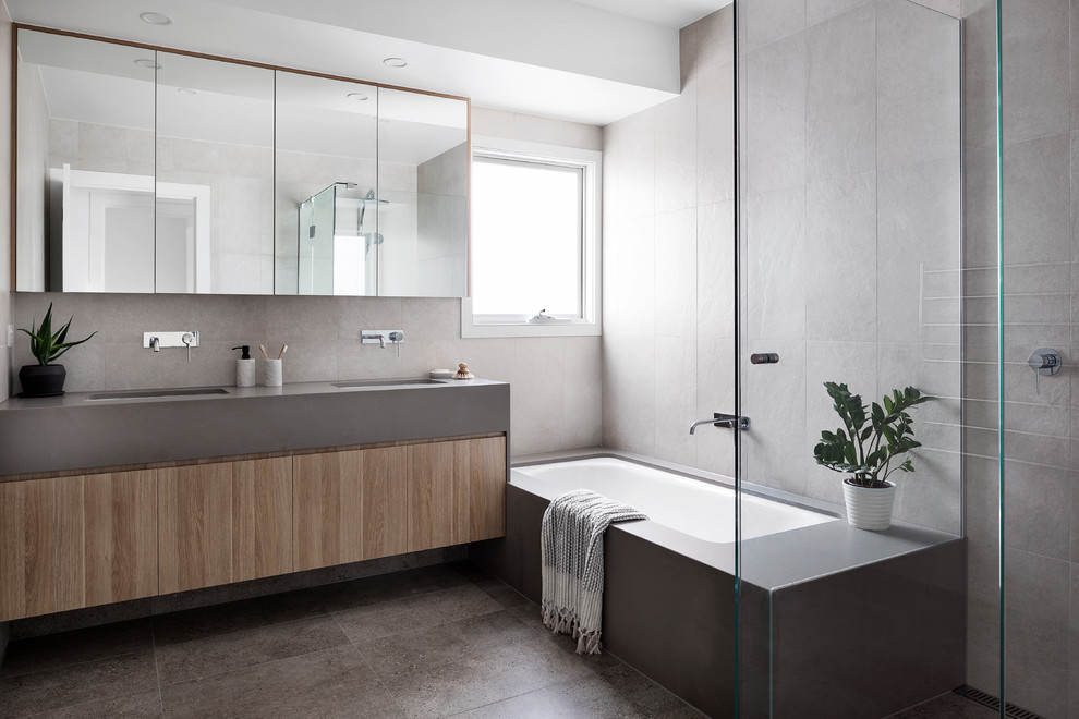 Inspiration for a mid-sized contemporary kids bathroom in Melbourne with flat-panel cabinets, light wood cabinets, a drop-in tub, white tile, white walls, a drop-in sink, concrete benchtops, grey benchtops, a corner shower, porcelain tile, porcelain floors, grey floor and a hinged shower door.