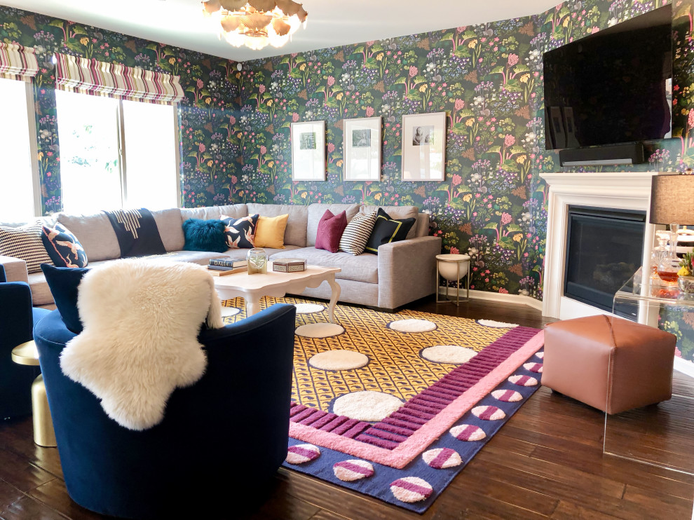 Modelo de sala de estar abierta bohemia de tamaño medio con chimenea de esquina, televisor colgado en la pared, papel pintado y suelo de madera oscura