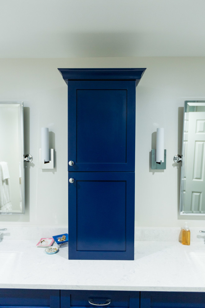 This is an example of a large transitional master bathroom in DC Metro with shaker cabinets, blue cabinets, an alcove tub, a corner shower, a two-piece toilet, white tile, marble, beige walls, plywood floors, an undermount sink, marble benchtops, brown floor, a hinged shower door and white benchtops.