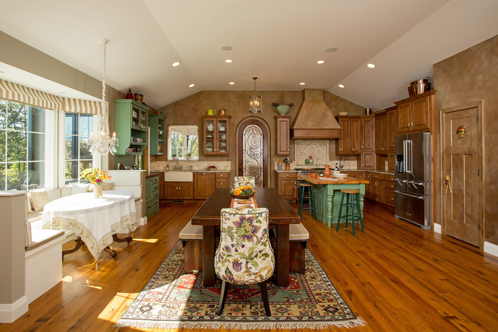 This is an example of a traditional l-shaped eat-in kitchen in DC Metro with a farmhouse sink, raised-panel cabinets, stainless steel appliances, with island, distressed cabinets, granite benchtops, beige splashback, limestone splashback, light hardwood floors and multi-coloured floor.