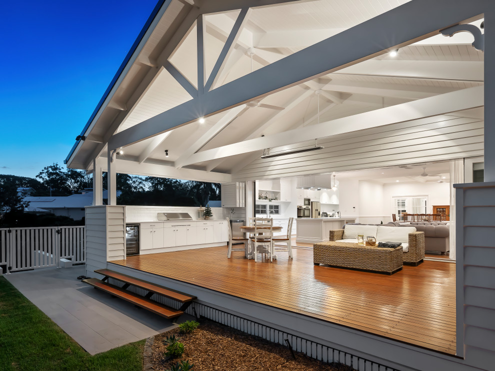 Example of a large classic backyard ground level wood railing outdoor kitchen deck design in Brisbane with a roof extension