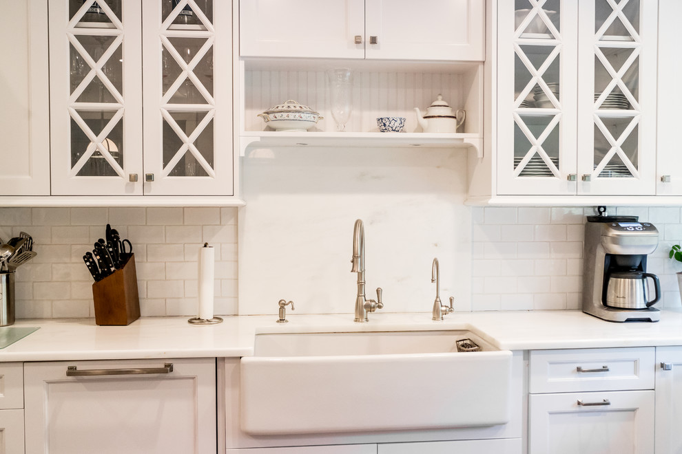 Mid-sized transitional dark wood floor and brown floor enclosed kitchen photo in New York with a farmhouse sink, recessed-panel cabinets, white cabinets, quartzite countertops, white backsplash, subway tile backsplash, stainless steel appliances and an island