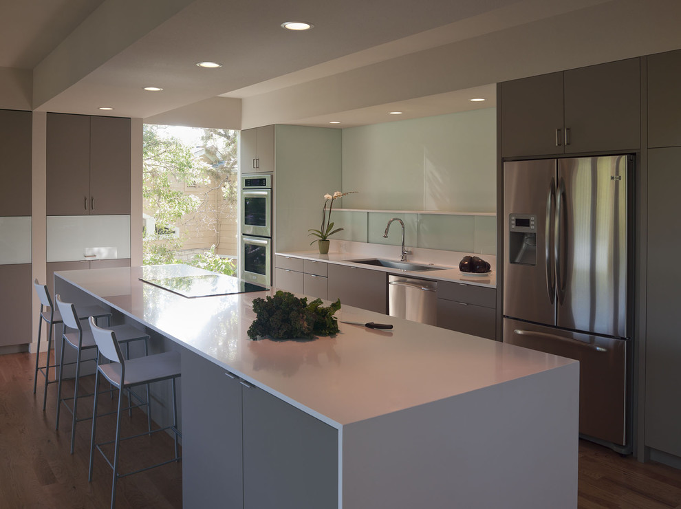 Design ideas for a large modern galley kitchen in Austin with stainless steel appliances, an undermount sink, flat-panel cabinets, grey cabinets, glass sheet splashback, white splashback, medium hardwood floors and with island.