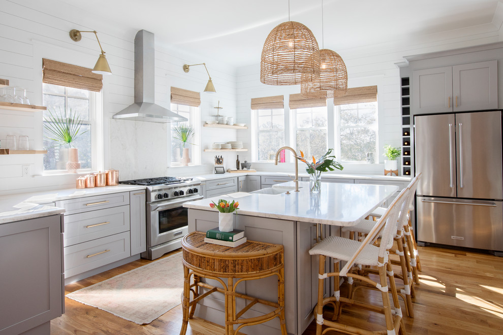 Design ideas for a beach style u-shaped kitchen in Charleston with a farmhouse sink, shaker cabinets, grey cabinets, white splashback, stainless steel appliances, medium hardwood floors, with island, brown floor and white benchtop.