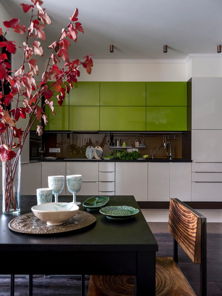 Inspiration for a mid-sized eclectic single-wall open plan kitchen in Moscow with a double-bowl sink, flat-panel cabinets, green cabinets, brown splashback, glass sheet splashback, stainless steel appliances, dark hardwood floors, brown floor and black benchtop.