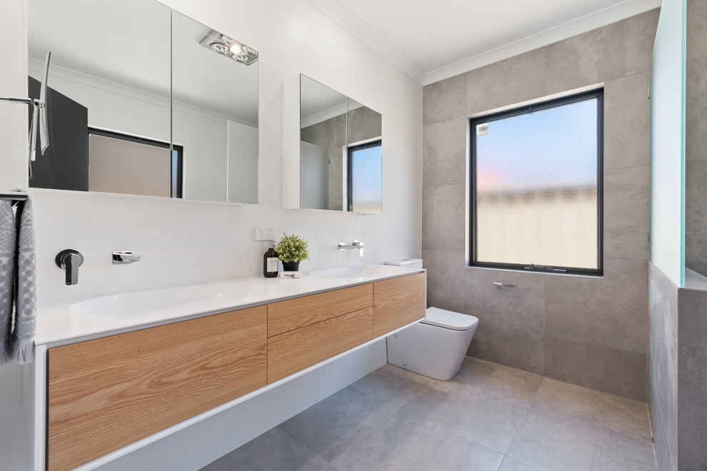 This is an example of a contemporary 3/4 bathroom in Perth with flat-panel cabinets, medium wood cabinets, gray tile, white walls, an integrated sink, grey floor and white benchtops.