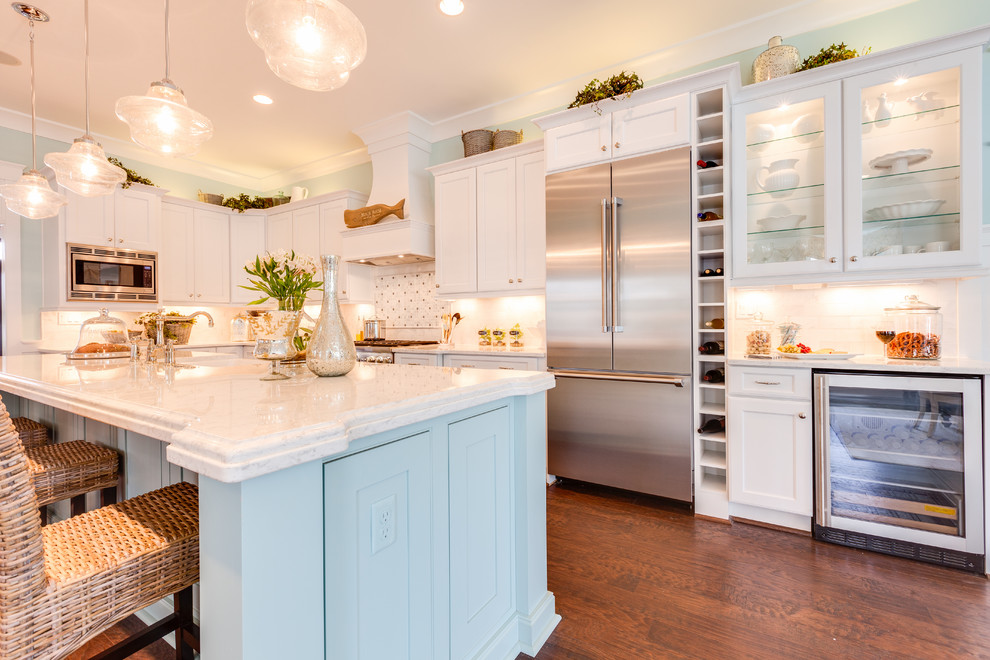 Design ideas for a large beach style l-shaped kitchen in Other with a farmhouse sink, recessed-panel cabinets, blue cabinets, marble benchtops, white splashback, stone tile splashback, dark hardwood floors, with island and stainless steel appliances.