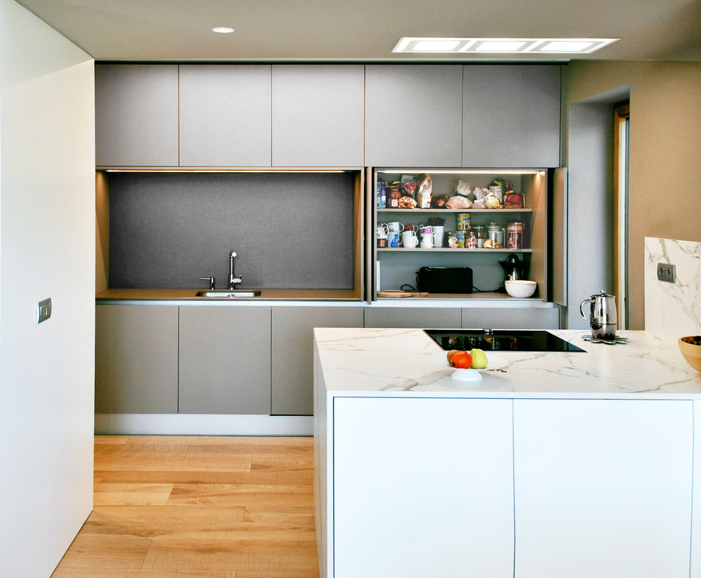 Photo of a mid-sized modern single-wall open plan kitchen in Other with an undermount sink, flat-panel cabinets, grey cabinets, quartzite benchtops, grey splashback, panelled appliances, medium hardwood floors, a peninsula and brown floor.