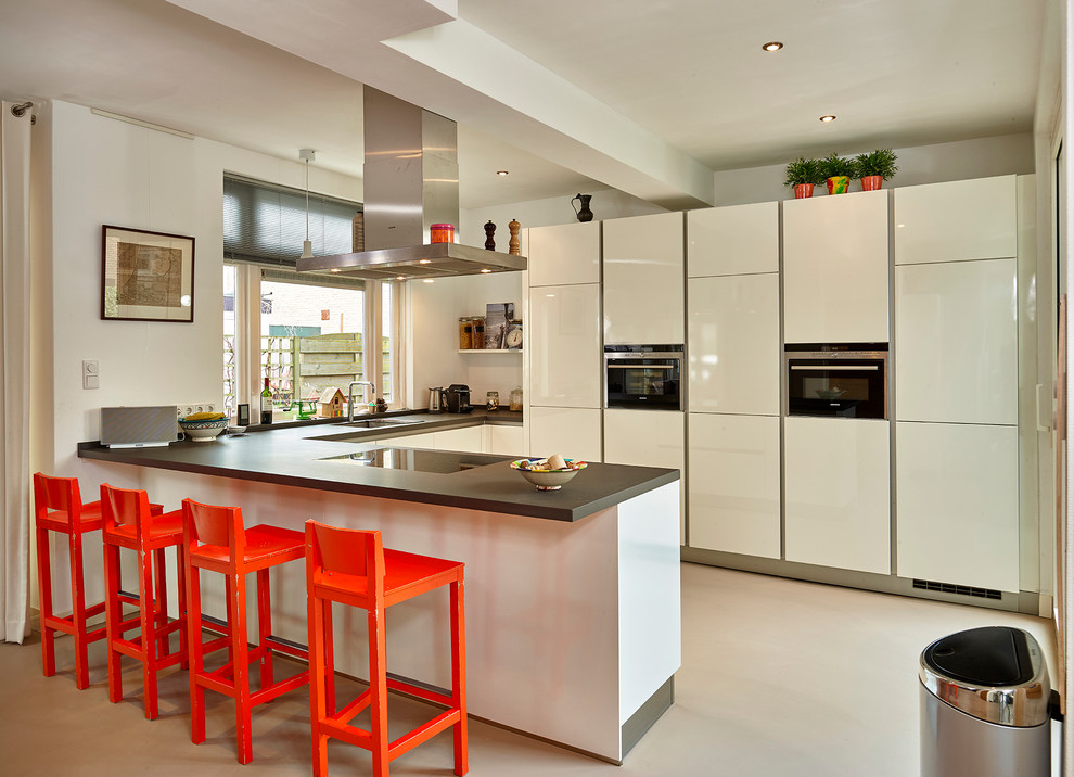 Photo of a large contemporary u-shaped eat-in kitchen in Other with a drop-in sink, flat-panel cabinets, white cabinets, granite benchtops, black appliances and a peninsula.
