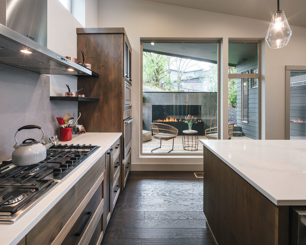Photo of a mid-sized country u-shaped eat-in kitchen in Portland with a drop-in sink, shaker cabinets, brown cabinets, quartz benchtops, grey splashback, ceramic splashback, stainless steel appliances, dark hardwood floors, with island, brown floor and white benchtop.