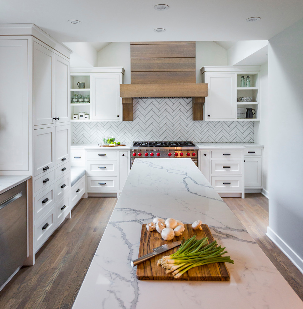 Inspiration for a country l-shaped kitchen in Cincinnati with an undermount sink, white cabinets, quartz benchtops, white splashback, porcelain splashback, stainless steel appliances, medium hardwood floors, with island, brown floor, white benchtop and shaker cabinets.