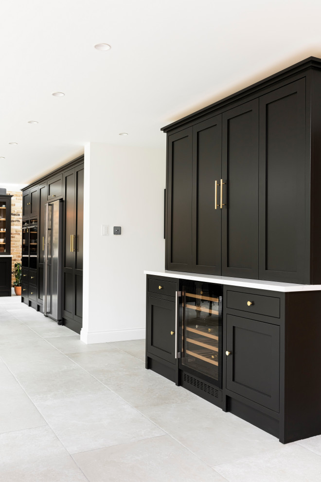 This is an example of a large traditional single-wall eat-in kitchen in London with a farmhouse sink, shaker cabinets, black cabinets, quartzite benchtops, black appliances, porcelain floors, with island, grey floor and white benchtop.