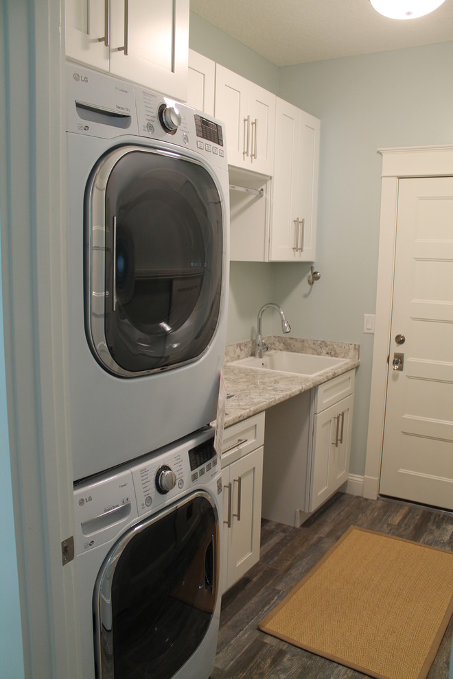Exempel på en mellanstor modern linjär tvättstuga enbart för tvätt, med en nedsänkt diskho, släta luckor, vita skåp, laminatbänkskiva, blå väggar, mellanmörkt trägolv och en tvättpelare