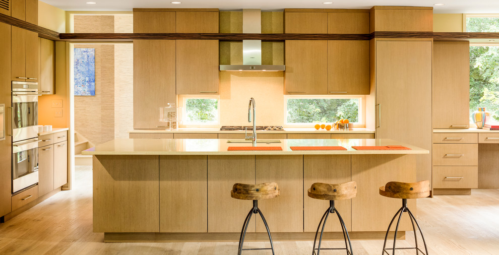 Photo of a contemporary l-shaped open plan kitchen in DC Metro with an undermount sink, flat-panel cabinets, medium wood cabinets, solid surface benchtops, glass sheet splashback and panelled appliances.