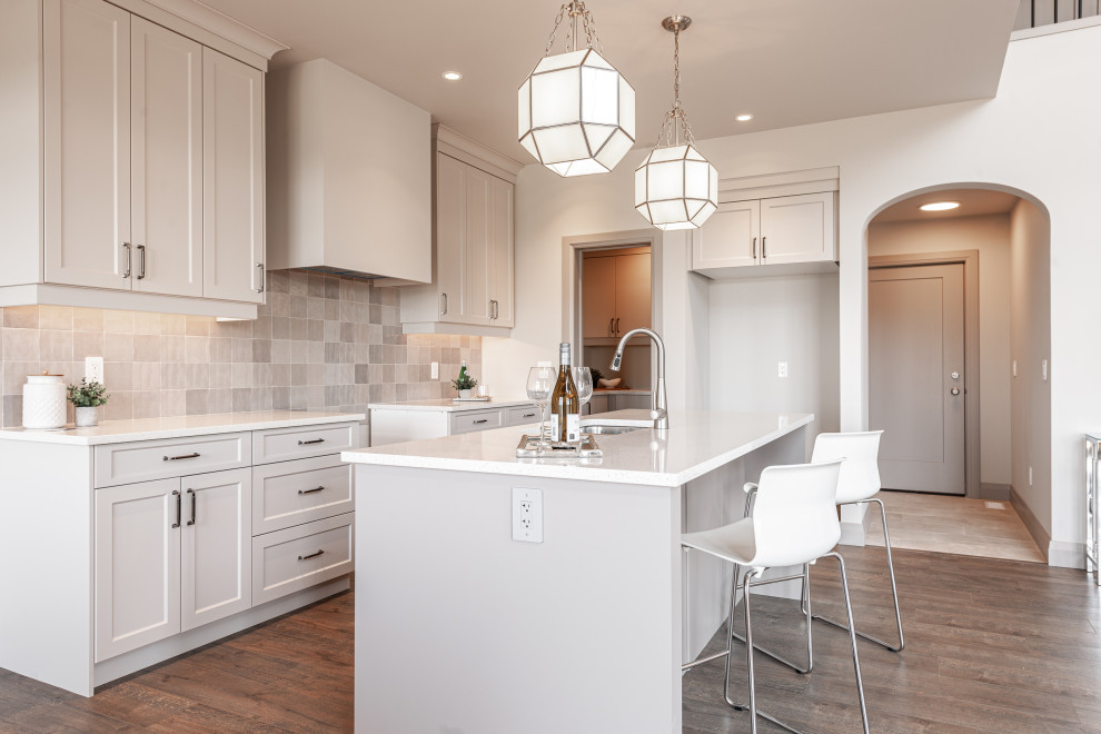 Inspiration for a small transitional galley laminate floor and brown floor open concept kitchen remodel in Toronto with a double-bowl sink, recessed-panel cabinets, beige cabinets, quartz countertops, beige backsplash, porcelain backsplash, stainless steel appliances, an island and white countertops