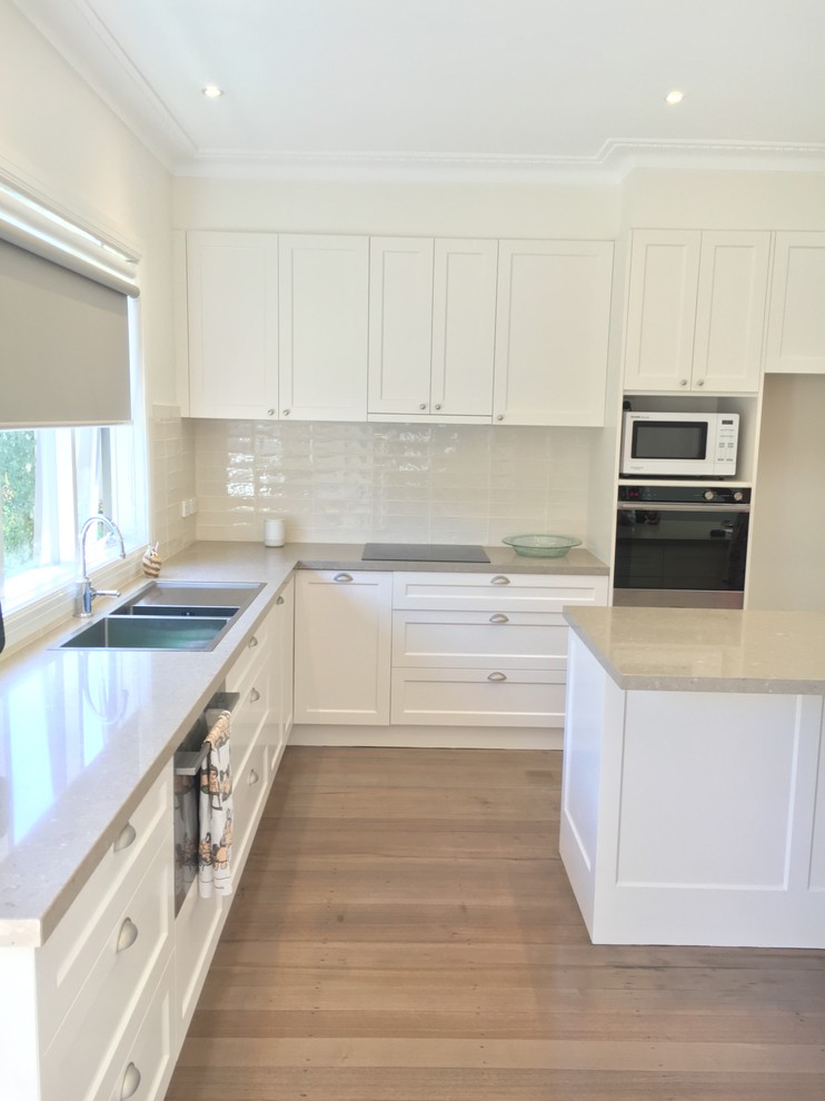 This is an example of a large traditional l-shaped kitchen in Melbourne with a double-bowl sink, shaker cabinets, limestone benchtops, beige splashback, subway tile splashback, stainless steel appliances, dark hardwood floors and with island.