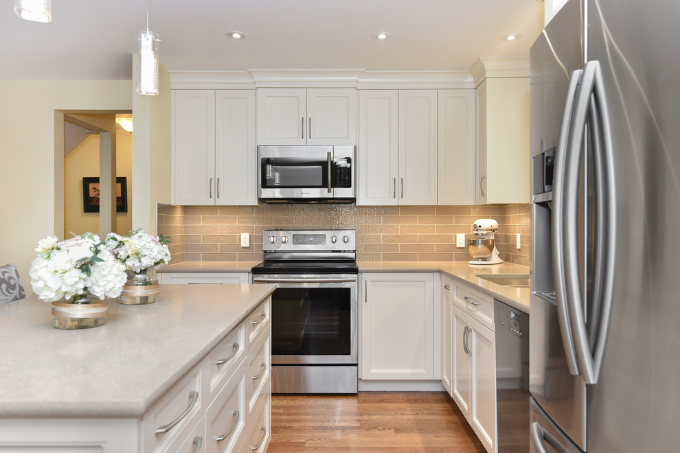 Eat-in kitchen - mid-sized transitional l-shaped medium tone wood floor and beige floor eat-in kitchen idea in Calgary with an undermount sink, recessed-panel cabinets, white cabinets, quartz countertops, gray backsplash, glass tile backsplash, stainless steel appliances and an island