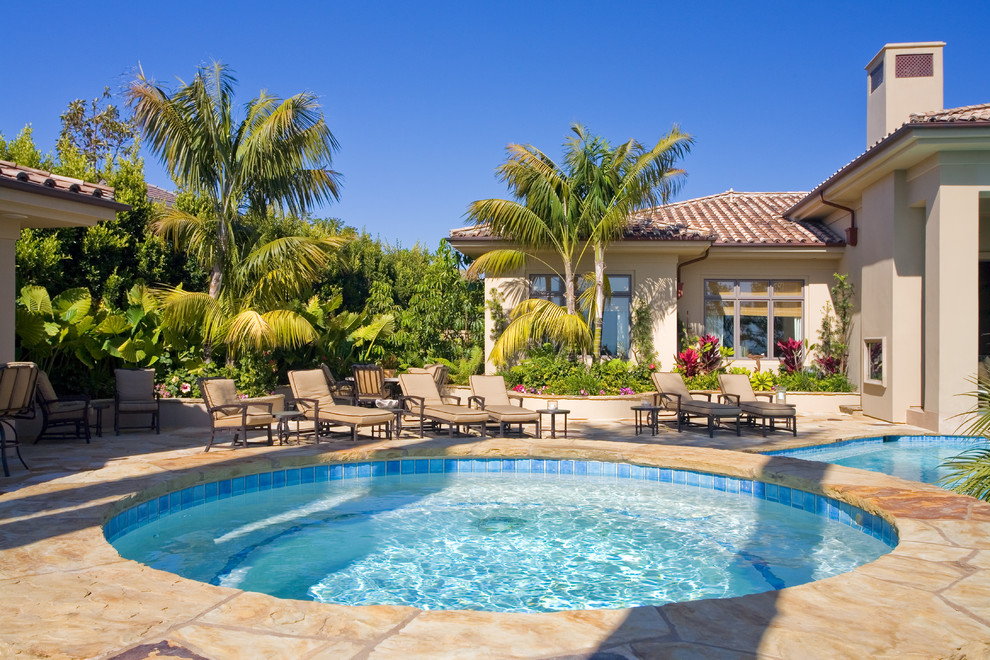 Large tropical backyard round natural pool in Orange County with a pool house and natural stone pavers.