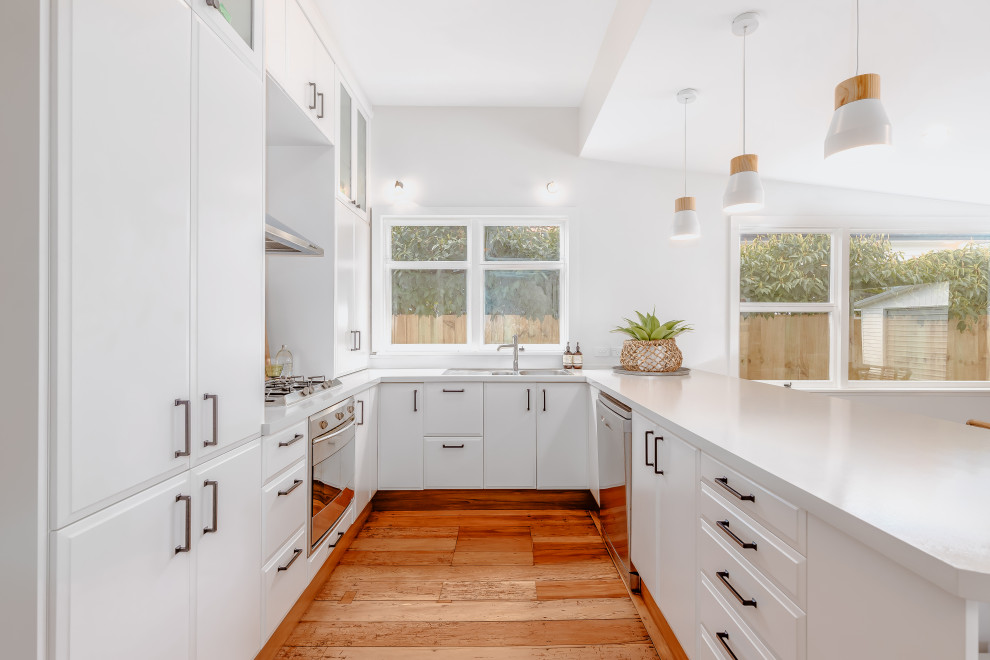 Bild på ett stort funkis grå grått kök, med en dubbel diskho, luckor med upphöjd panel, laminatbänkskiva, rostfria vitvaror, en halv köksö, vita skåp, mellanmörkt trägolv och brunt golv