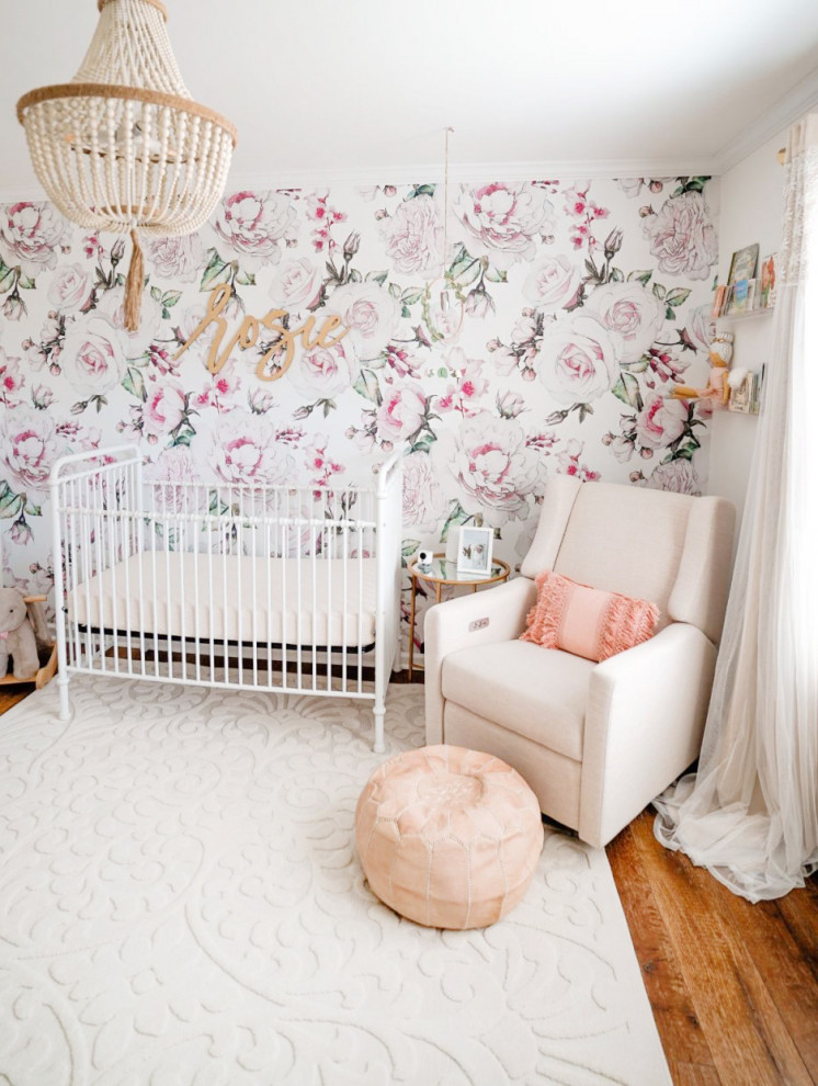 Diseño de habitación de bebé niña actual de tamaño medio con paredes blancas, suelo de madera en tonos medios, suelo marrón y papel pintado