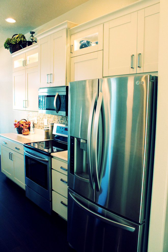 Example of a transitional galley eat-in kitchen design in Boise with an integrated sink, shaker cabinets, white cabinets, solid surface countertops, beige backsplash, glass tile backsplash and stainless steel appliances