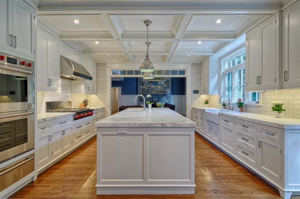 Large elegant galley medium tone wood floor and brown floor kitchen pantry photo in New York with white cabinets, marble countertops, white backsplash, stainless steel appliances, an island, subway tile backsplash, a farmhouse sink and shaker cabinets