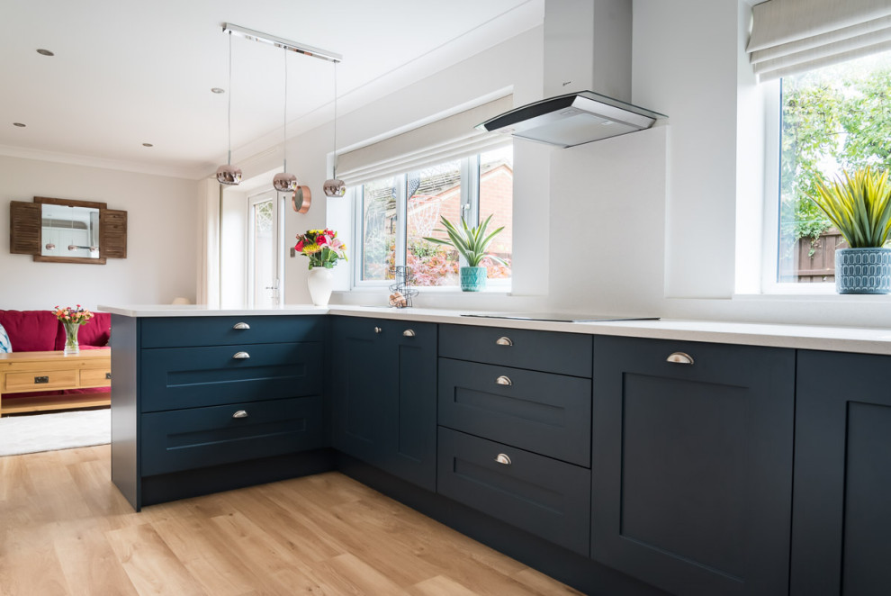 Photo of a mid-sized traditional u-shaped eat-in kitchen in Berkshire with a double-bowl sink, shaker cabinets, blue cabinets, quartzite benchtops, white splashback, black appliances, linoleum floors, a peninsula, brown floor and white benchtop.