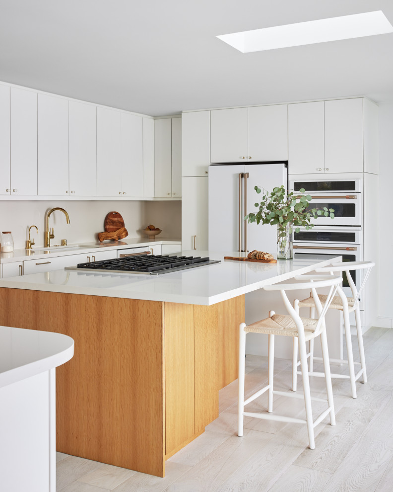 Large midcentury u-shaped open plan kitchen in Los Angeles with an undermount sink, flat-panel cabinets, white cabinets, quartz benchtops, white splashback, engineered quartz splashback, white appliances, light hardwood floors, with island, beige floor and white benchtop.