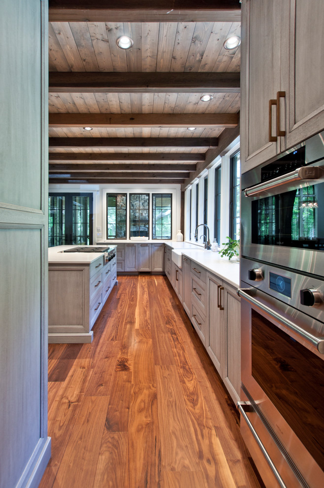 Inspiration for a large transitional medium tone wood floor and brown floor open concept kitchen remodel in Nashville with a farmhouse sink, flat-panel cabinets, gray cabinets, quartz countertops, stainless steel appliances, an island and white countertops