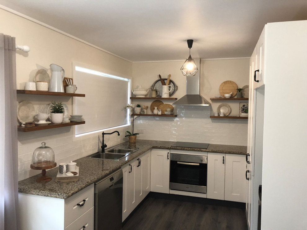 This is an example of a mid-sized country u-shaped kitchen pantry in Brisbane with a double-bowl sink, shaker cabinets, white cabinets, granite benchtops, white splashback, porcelain splashback, stainless steel appliances, laminate floors, no island, brown floor and brown benchtop.