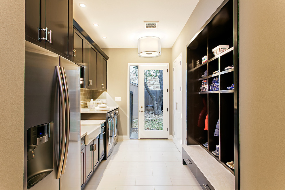 Inspiration for a transitional laundry room in Austin with a farmhouse sink, black cabinets, marble benchtops, beige walls, porcelain floors and a side-by-side washer and dryer.
