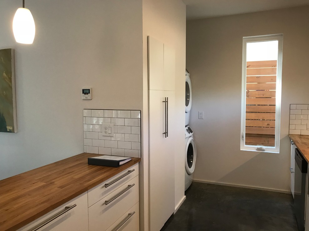 Small modern single-wall utility room in Atlanta with white walls, concrete floors, a stacked washer and dryer and grey floor.