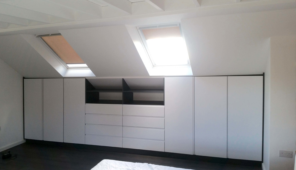 This is an example of a mid-sized modern storage and wardrobe in London with white cabinets, laminate floors and black floor.