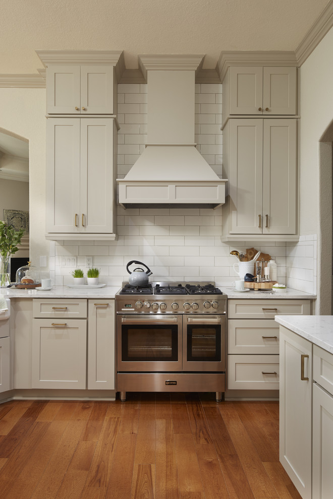 Enclosed kitchen - mid-sized transitional u-shaped medium tone wood floor and brown floor enclosed kitchen idea in Atlanta with a farmhouse sink, shaker cabinets, gray cabinets, quartz countertops, white backsplash, subway tile backsplash, stainless steel appliances, a peninsula and white countertops