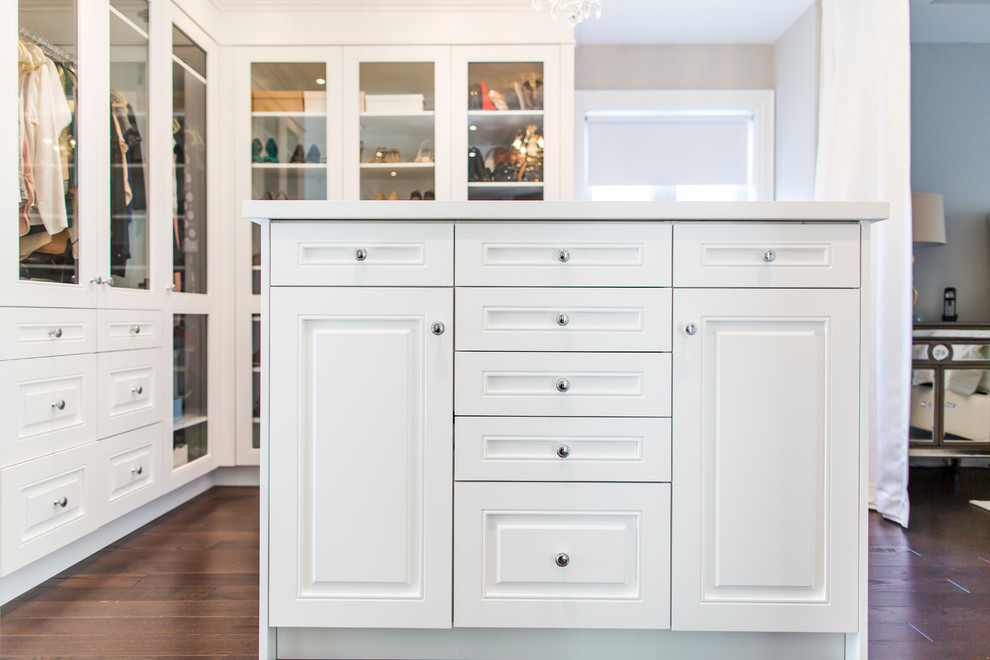 Large transitional gender-neutral walk-in wardrobe in Toronto with raised-panel cabinets, white cabinets and dark hardwood floors.