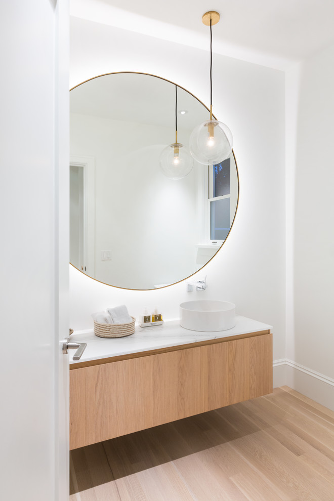 Design ideas for a mid-sized transitional powder room in Vancouver with flat-panel cabinets, light wood cabinets, white walls, light hardwood floors and marble benchtops.