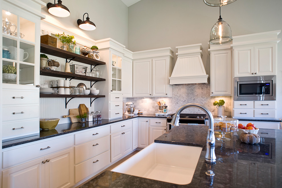 Mid-sized transitional l-shaped light wood floor and brown floor open concept kitchen photo with a farmhouse sink, raised-panel cabinets, white cabinets, granite countertops, multicolored backsplash, mosaic tile backsplash, stainless steel appliances and an island