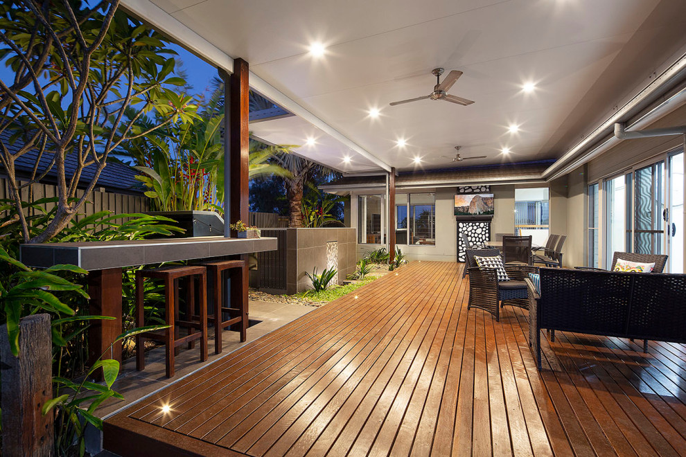 Photo of a tropical backyard partial sun garden in Sunshine Coast with a fire feature, decking and a wood fence.