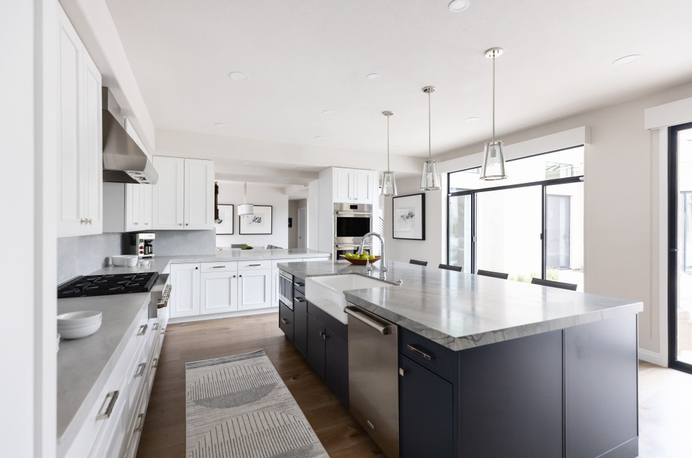 Large transitional medium tone wood floor and brown floor eat-in kitchen photo in Phoenix with a farmhouse sink, recessed-panel cabinets, white cabinets, quartzite countertops, beige backsplash, stone slab backsplash, paneled appliances, an island and gray countertops