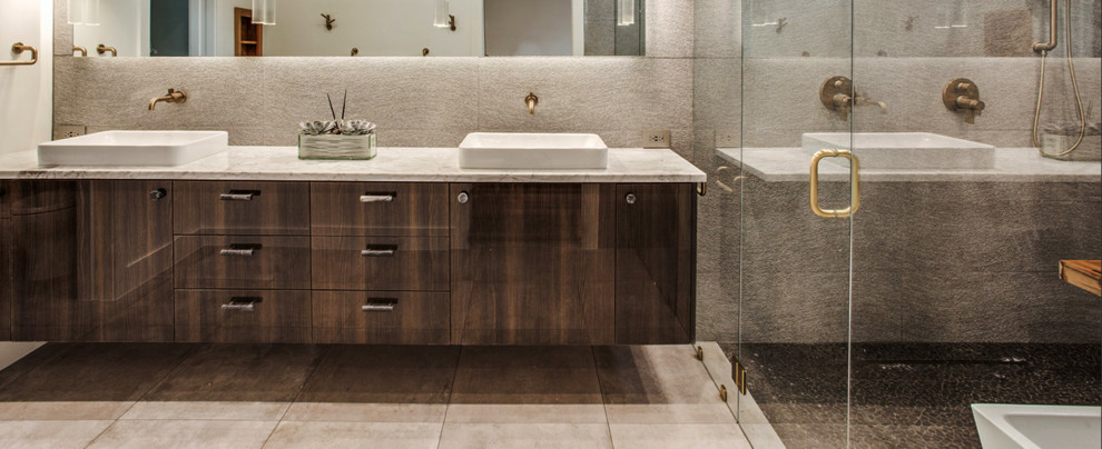This is an example of a large contemporary master wet room bathroom in Dallas with flat-panel cabinets, brown cabinets, a freestanding tub, gray tile, pebble tile, grey walls, porcelain floors, a drop-in sink, marble benchtops, grey floor, a hinged shower door and grey benchtops.