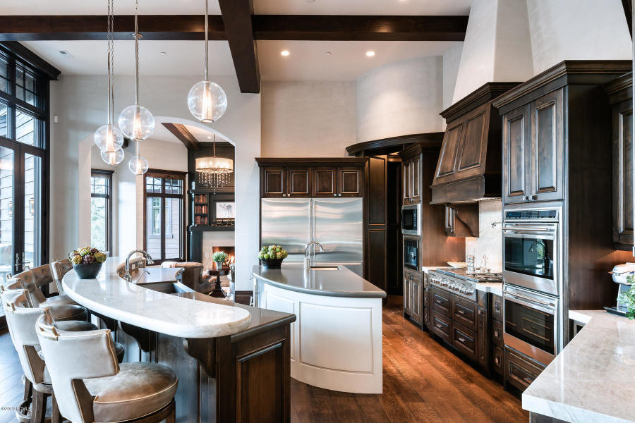 This is an example of a large transitional l-shaped eat-in kitchen in Salt Lake City with a farmhouse sink, raised-panel cabinets, dark wood cabinets, limestone benchtops, white splashback, stone slab splashback, stainless steel appliances, dark hardwood floors, multiple islands, brown floor and white benchtop.