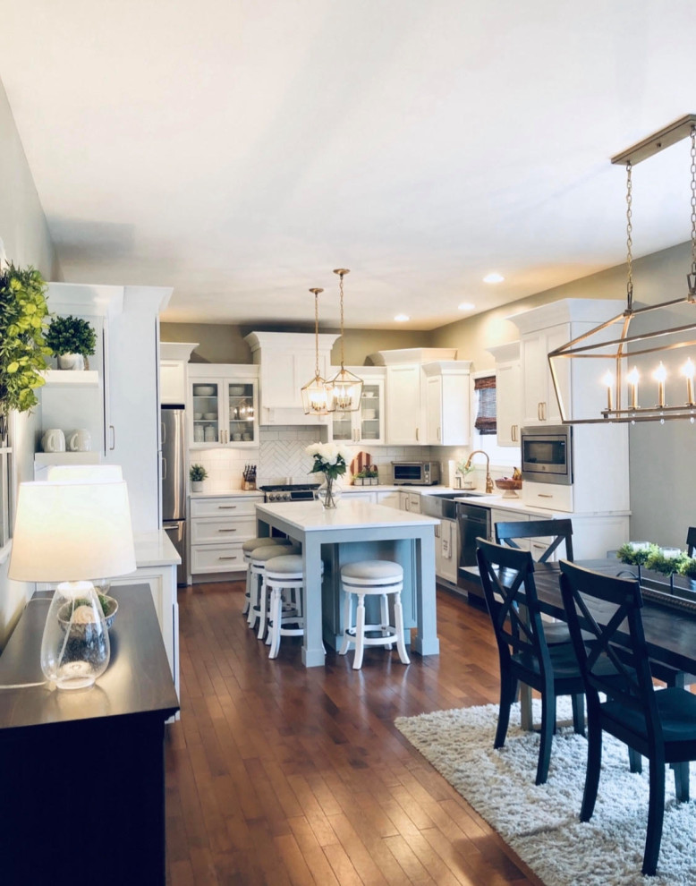 Inspiration for a mid-sized galley laminate floor and brown floor eat-in kitchen remodel in Other with a farmhouse sink, shaker cabinets, white cabinets, quartz countertops, white backsplash, porcelain backsplash, stainless steel appliances, an island and white countertops