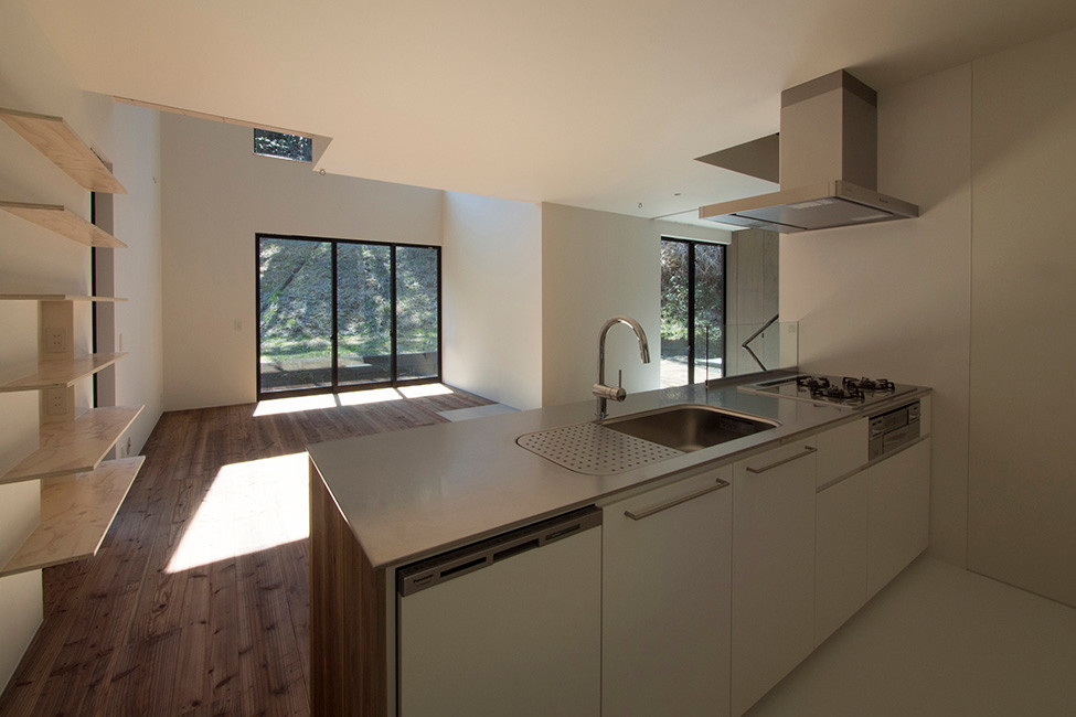 他の地域にある低価格の中くらいなモダンスタイルのおしゃれなキッチン (一体型シンク、フラットパネル扉のキャビネット、白いキャビネット、ステンレスカウンター、白いキッチンパネル、ガラス板のキッチンパネル、シルバーの調理設備、クッションフロア) の写真