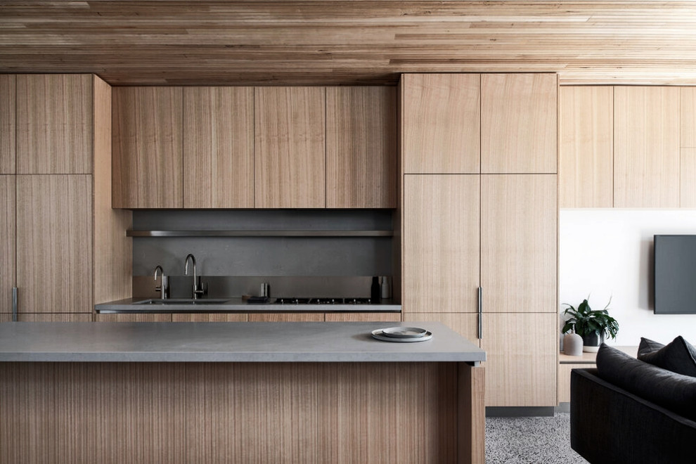 This is an example of a mid-sized scandinavian galley open plan kitchen in Melbourne with an undermount sink, flat-panel cabinets, light wood cabinets, quartz benchtops, grey splashback, engineered quartz splashback, stainless steel appliances, concrete floors, with island and grey benchtop.