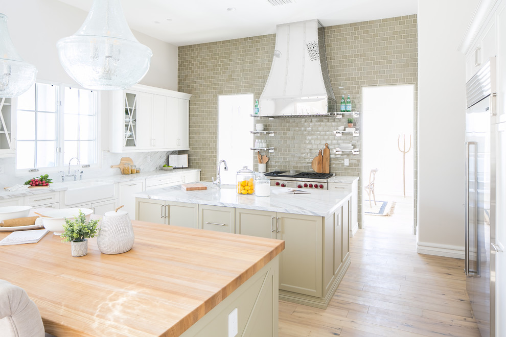 Large transitional light wood floor and brown floor eat-in kitchen photo in Phoenix with a farmhouse sink, white cabinets, marble countertops, green backsplash, ceramic backsplash, stainless steel appliances and two islands